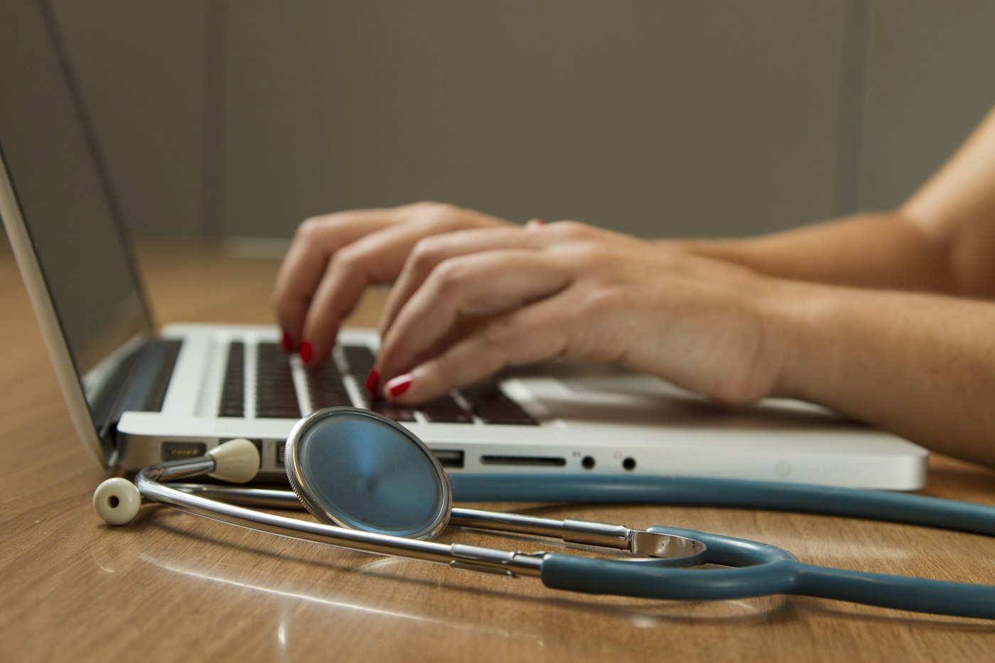 Hands on a laptop beside a stethoscope.