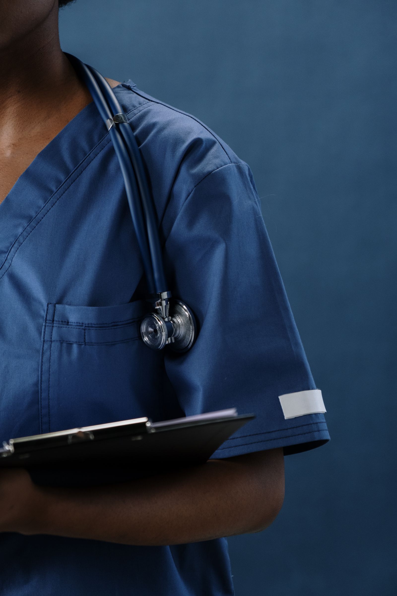 Clinician in navy scrubs with a stethoscope and clipboard.